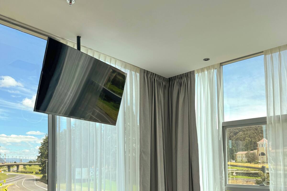 Ein Hotelzimmer mit einem großen Bett, einem an der Wand montierten Flachbildfernseher und Blick auf eine Autobahn und Grünfläche.