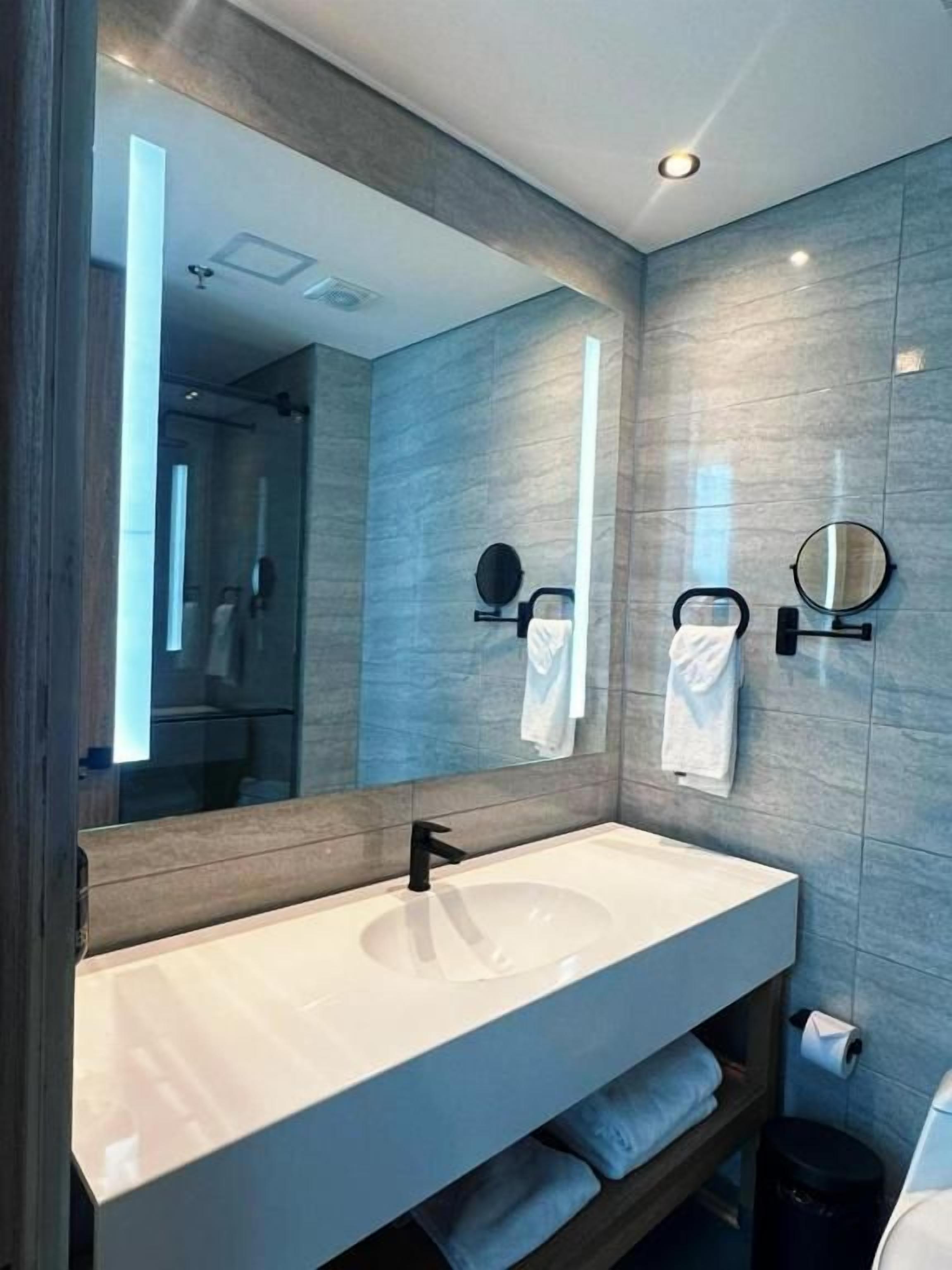 A modern bathroom with a large mirror, a white sink, and a towel rack.