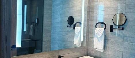 A modern bathroom with a large mirror, a white sink, and a towel rack.