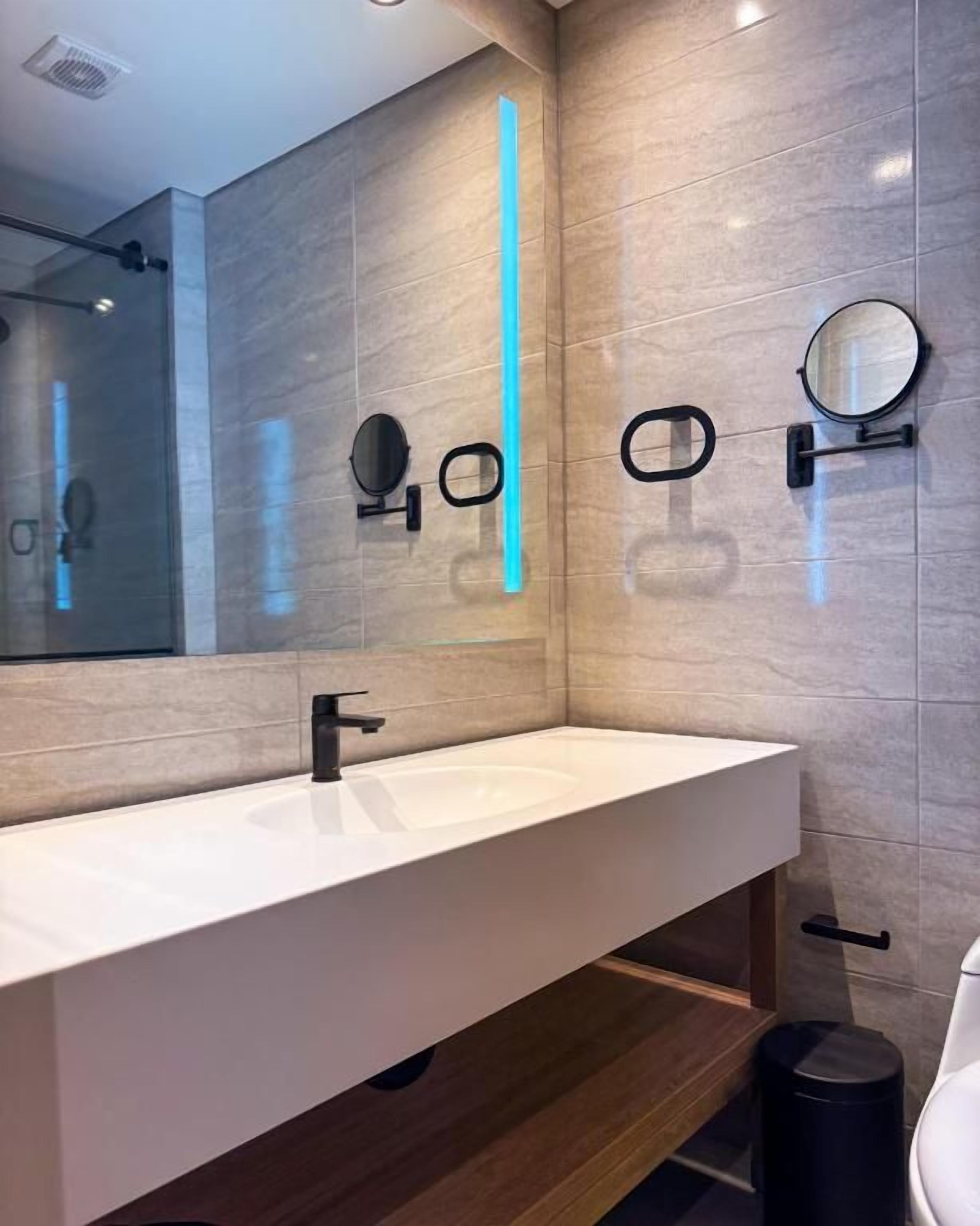 Een moderne badkamer met een wit wastafel, twee spiegels en een zwarte prullenbak.