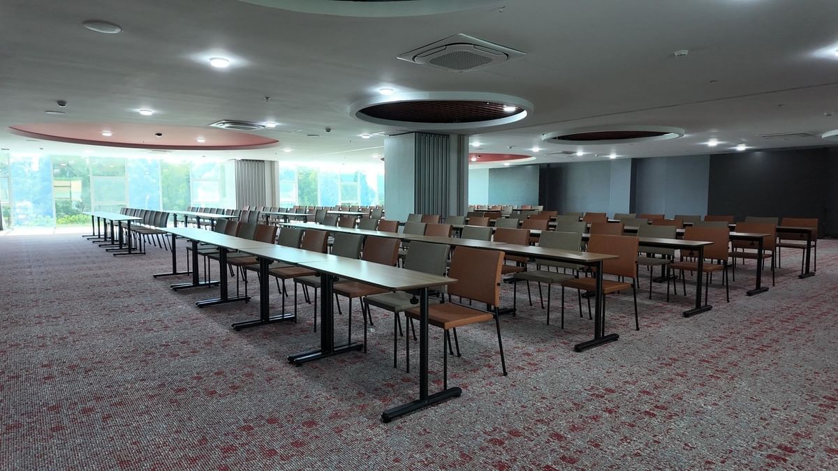 A conference room with long tables and chairs, large windows, and a carpeted floor.