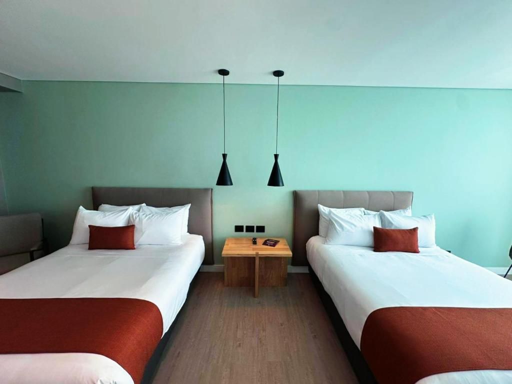 Habitación de hotel con dos camas, una mesita de madera y lámparas colgantes.