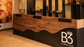 A hotel reception desk with a modern design, including a circular light fixture above and a large abstract painting on the wall. - Hotel B3 Sibelius (Chía)