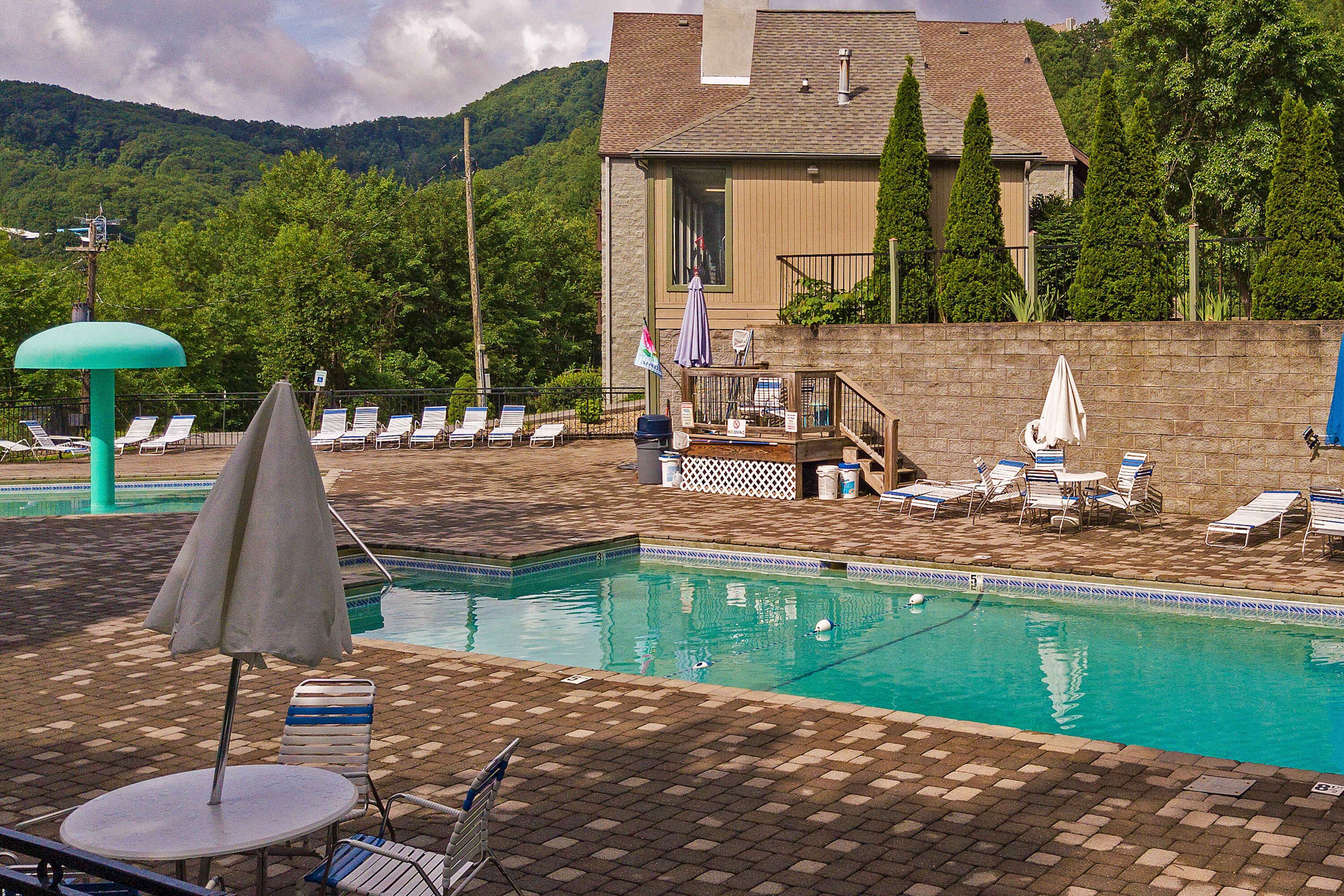 A swimming pool with lounge chairs and umbrellas, surrounded by a brick patio and a stone wall.