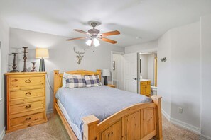 Ein Schlafzimmer mit einem Holzbett, einem Schminktisch, einem Deckenventilator und einem Hirschgeweih an der Wand.