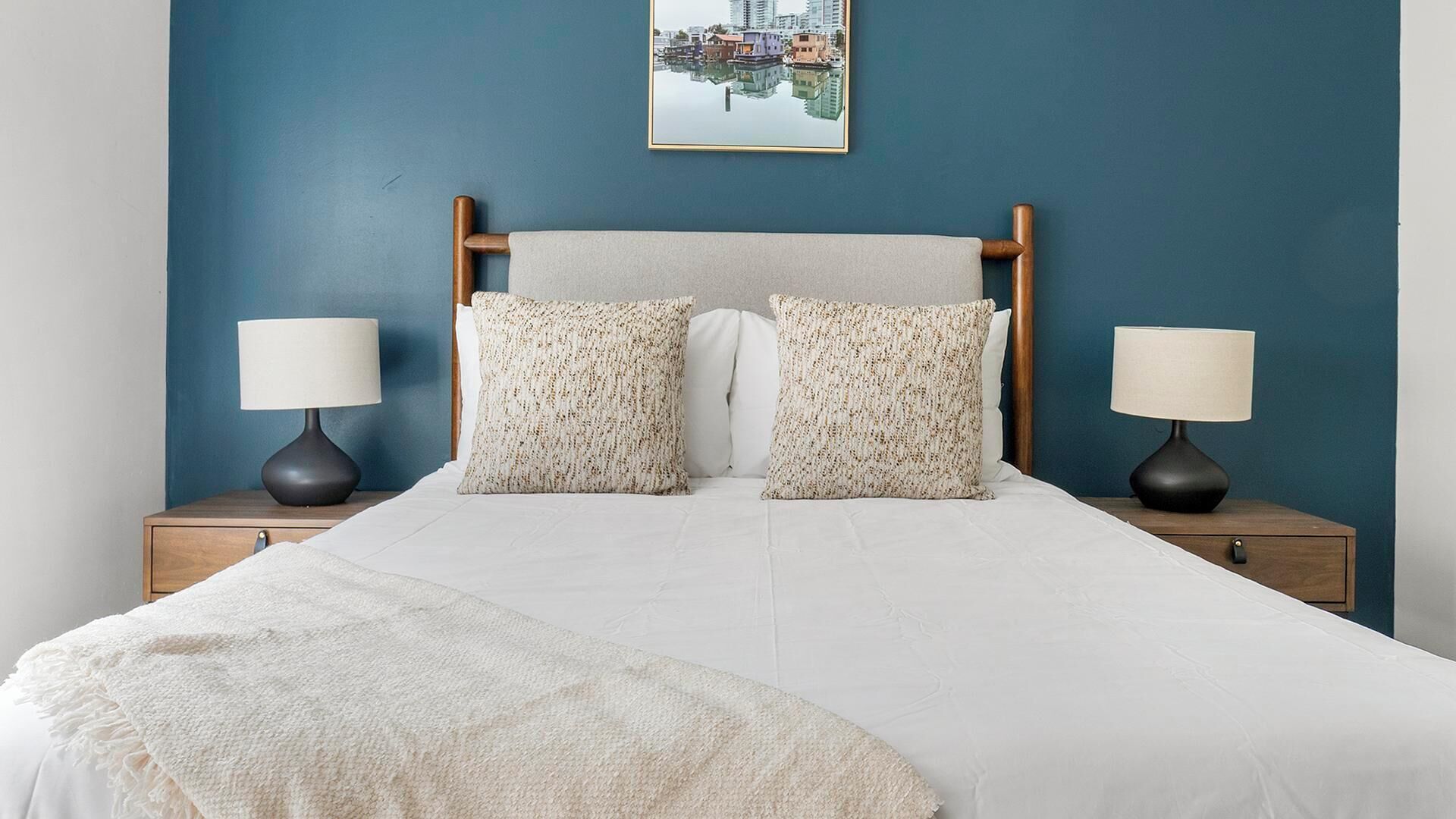 A neatly made bed with two pillows, two bedside tables with lamps, and a framed picture on the wall.