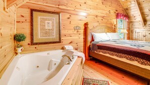 Une chambre dans une cabane en bois, avec un grand lit en bois, un plafond en bois et une baignoire blanche.