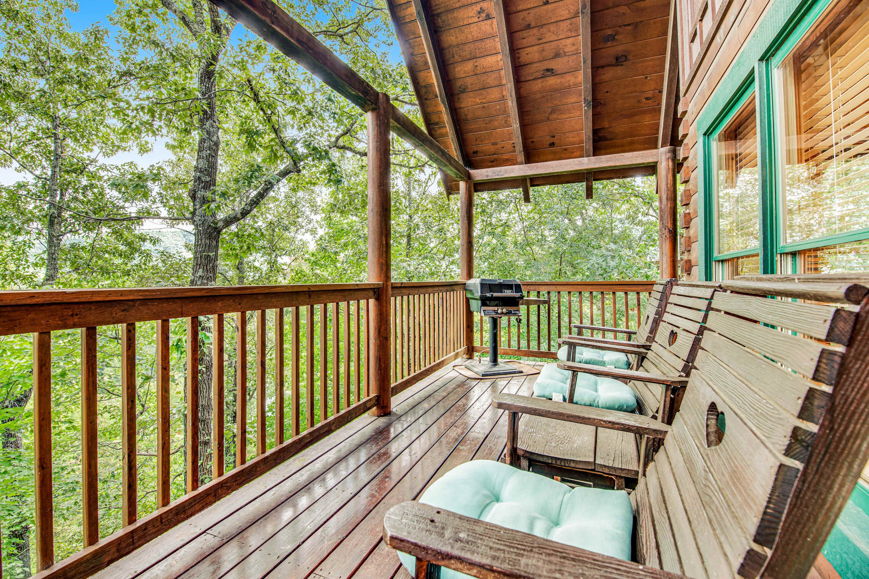 Une terrasse en bois avec un barbecue et un espace salon donnant sur une forêt.