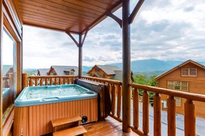 Eine Holzterrasse mit Whirlpool, Holzgeländern und Blick auf umliegende Blockhütten.