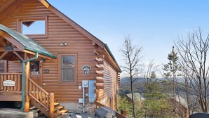 Une cabane en rondins de bois, dotée d’un porche, d’une boîte aux lettres et offrant une vue sur le paysage environnant.