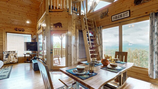 L’intérieur d’un chalet en bois comprend un coin repas, un téléviseur et un escalier menant à un étage supérieur.