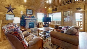 L’intérieur chaleureux d’un chalet avec une cheminée, des sièges confortables, un téléviseur et une décoration en forme d’étoile sur le mur.