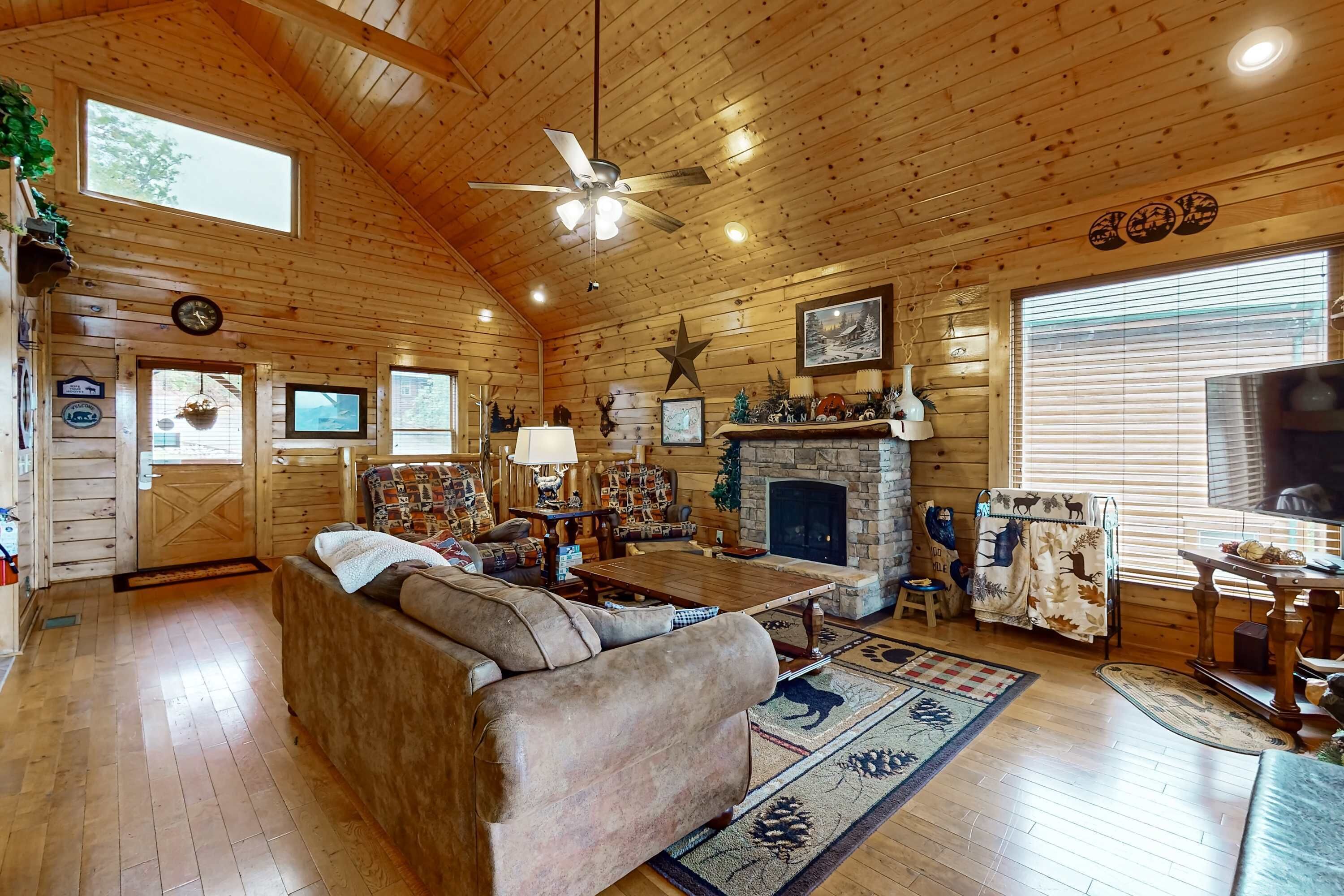 L’intérieur d’un chalet confortable, avec une cheminée, des meubles en bois et un ventilateur de plafond.