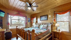 Une chambre rustique en bois, avec un grand lit, un ventilateur de plafond et de nombreuses fenêtres équipées de rideaux.