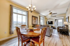 Un espace repas avec une table et des chaises en bois, un lustre et une vue sur l’extérieur.
