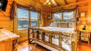 A wooden cabin bedroom with a bed, a ceiling fan, and large windows offering a mountain view. - Charming Log cabin, Sleeps 6・Game Room・Hot Tub (Pigeon Forge)