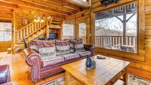 A wooden cabin interior with a leather sofa, wooden table, and a staircase leading to a balcony. - Charming Log cabin, Sleeps 6・Game Room・Hot Tub (Pigeon Forge)