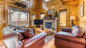 A cozy log cabin interior with leather sofas, a stone fireplace, and a television. - Charming Log cabin, Sleeps 6・Game Room・Hot Tub (Pigeon Forge)
