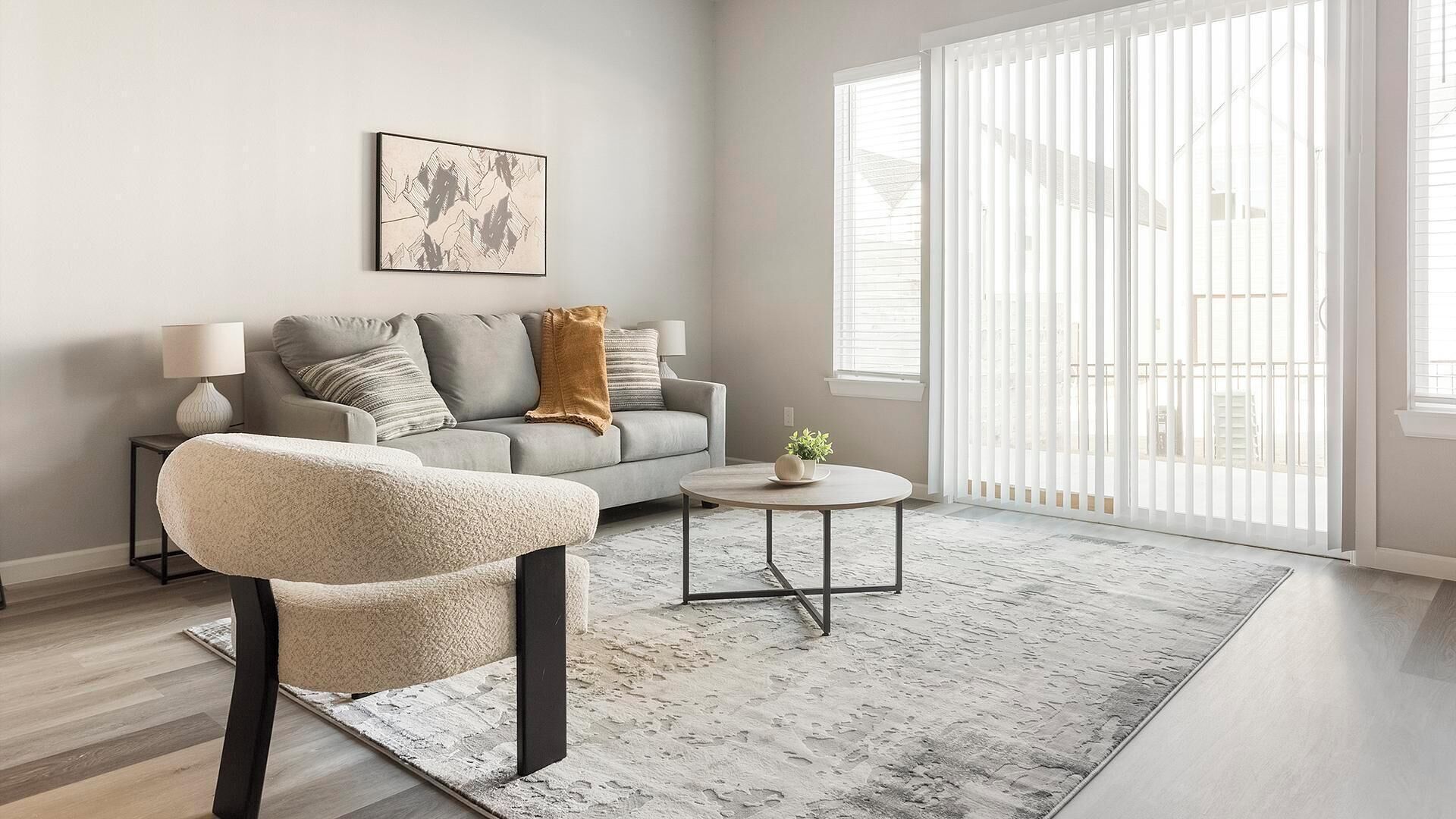 A modern living room with a grey sofa, a round coffee table, and a fluffy armchair.