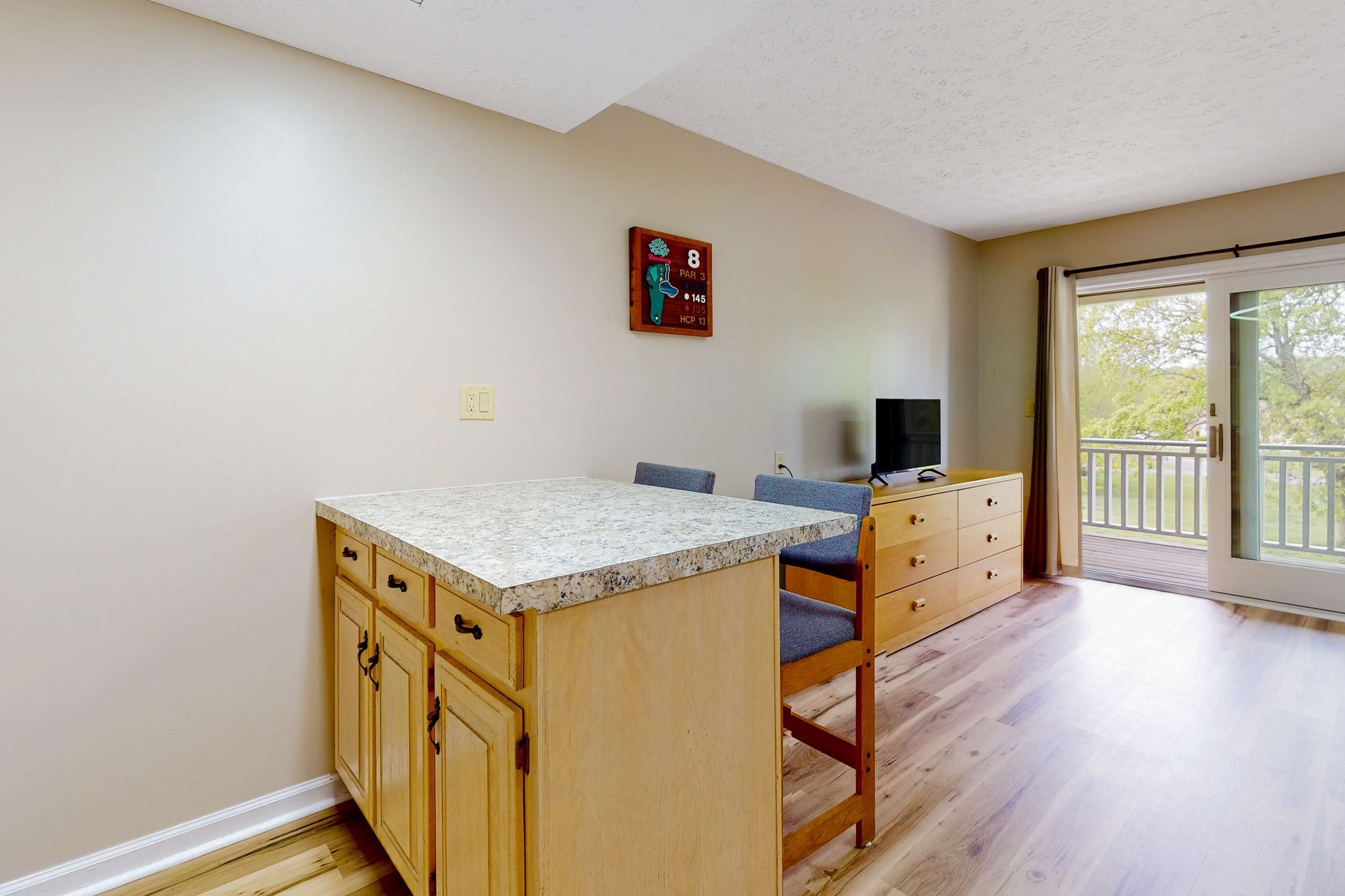 A kitchen with wooden cabinets, a granite countertop, and a dining area with a chair and a television.