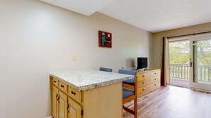 Una cocina con armarios de madera, encimera de granito y un comedor con una silla y un televisor.