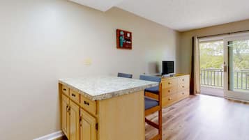 A kitchen with wooden cabinets, a granite countertop, and a dining area with a chair and a television.