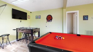Una habitación con mesa de billar, mesa de futbolín, dardos y televisor montado en la pared.