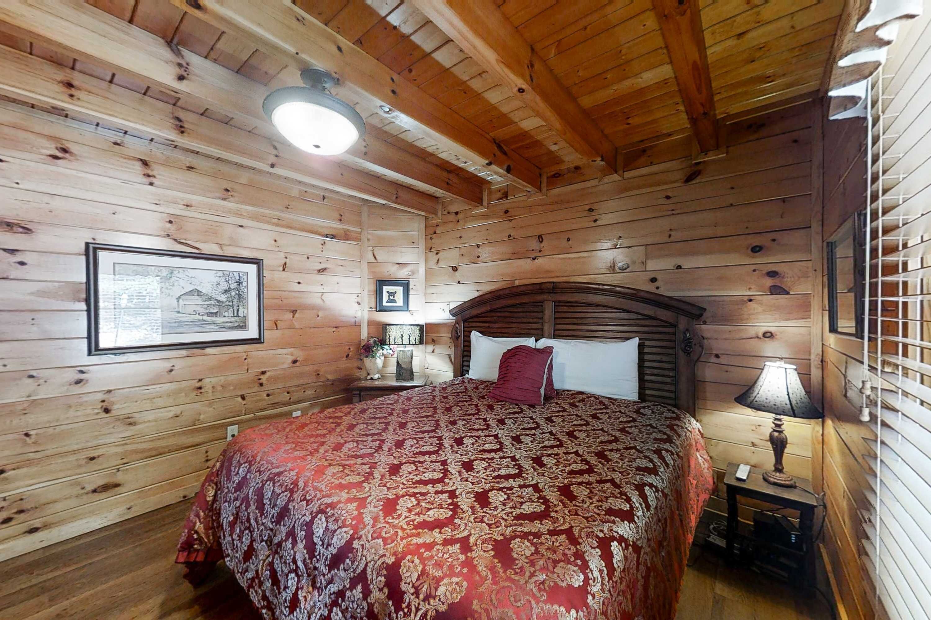 A wooden cabin bedroom with a bed, a nightstand, a lamp, and framed pictures on the walls.