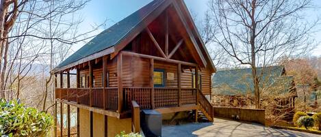 A wooden cabin with a balcony, a covered porch, and a small attached shed.