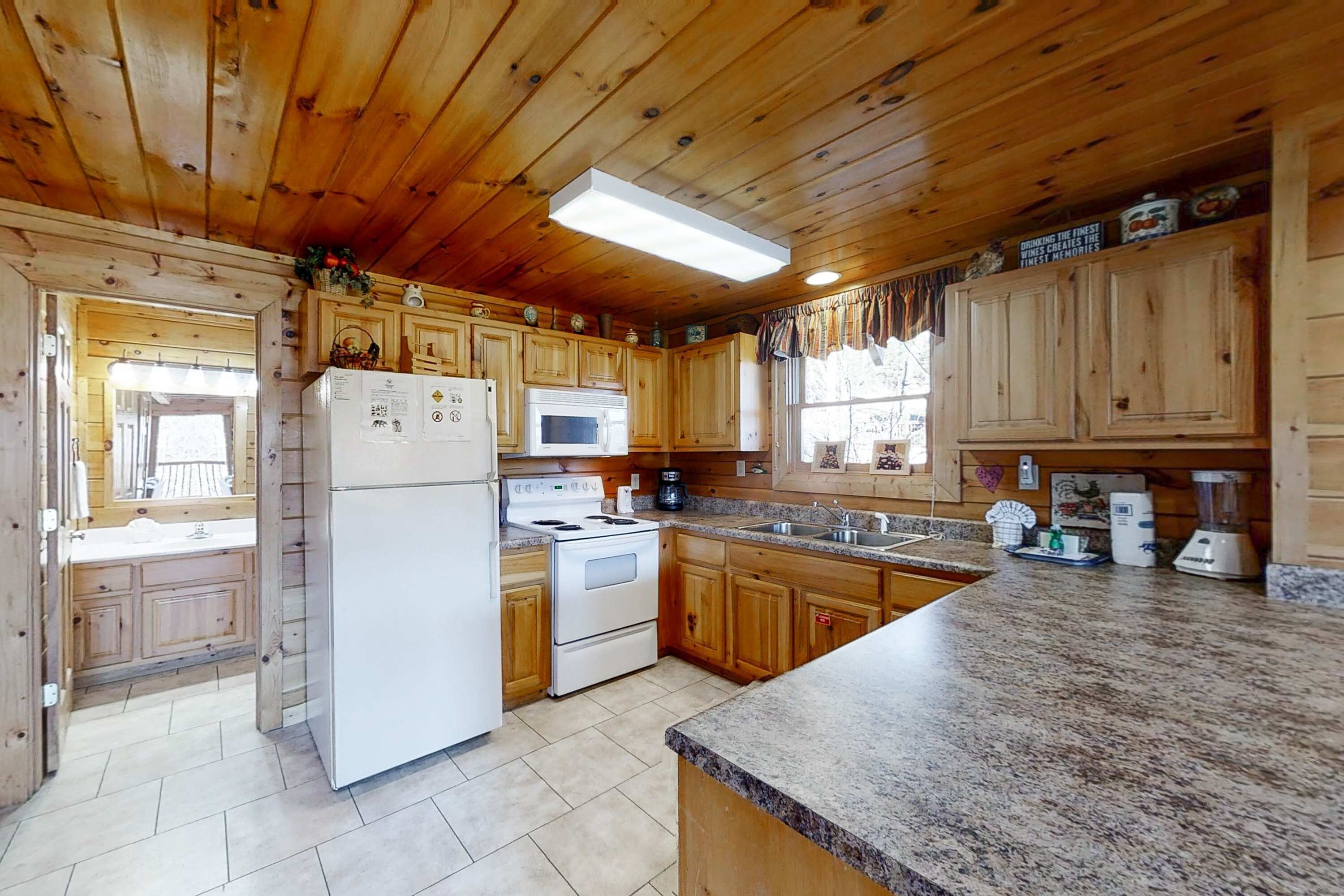 A wooden cabin kitchen with a refrigerator, stove, microwave, and granite countertop.