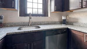 A kitchen with a granite countertop, stainless steel sink, and dark wooden cabinets. - Landing | Incredible 1BD, Courtyard, Gym (Baltimore)