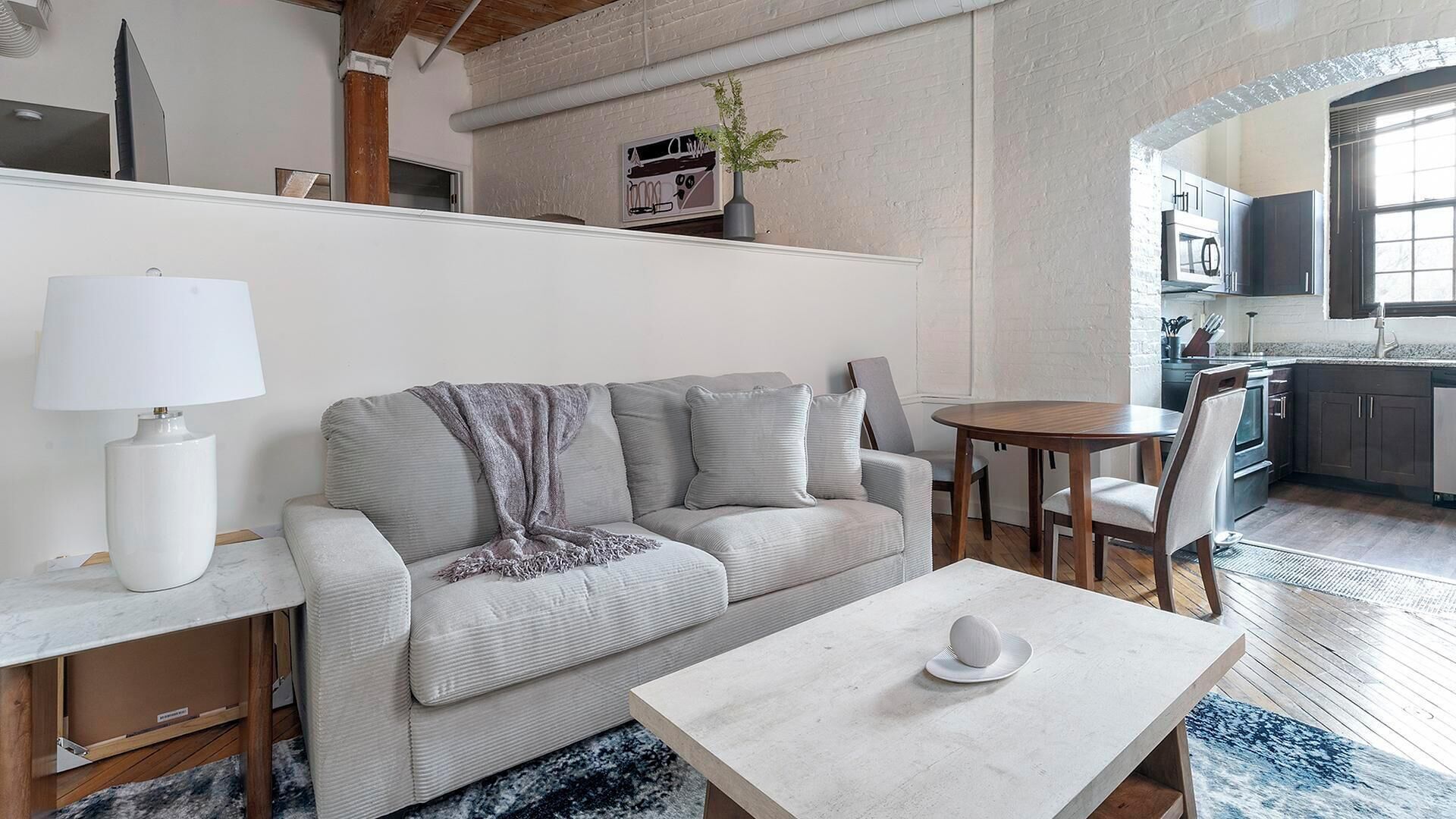 En moderne stue med en grå sofa, et hvidt sofabord og et spiseområde med et rundt bord og stole.