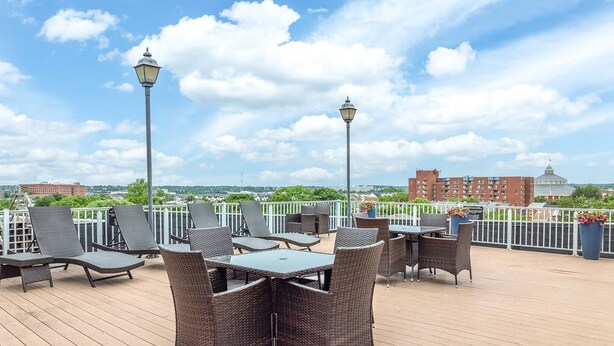 A rooftop terrace with wicker furniture, tables, and chairs, overlooking a cityscape with buildings and a dome structure. - Landing | Incredible 1BD, Courtyard, Gym (Baltimore)