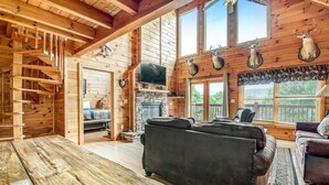 L’intérieur d’une cabane en rondins, avec une cheminée, des canapés en cuir, une cheminée en pierre et des têtes de cerf accrochées au mur.
