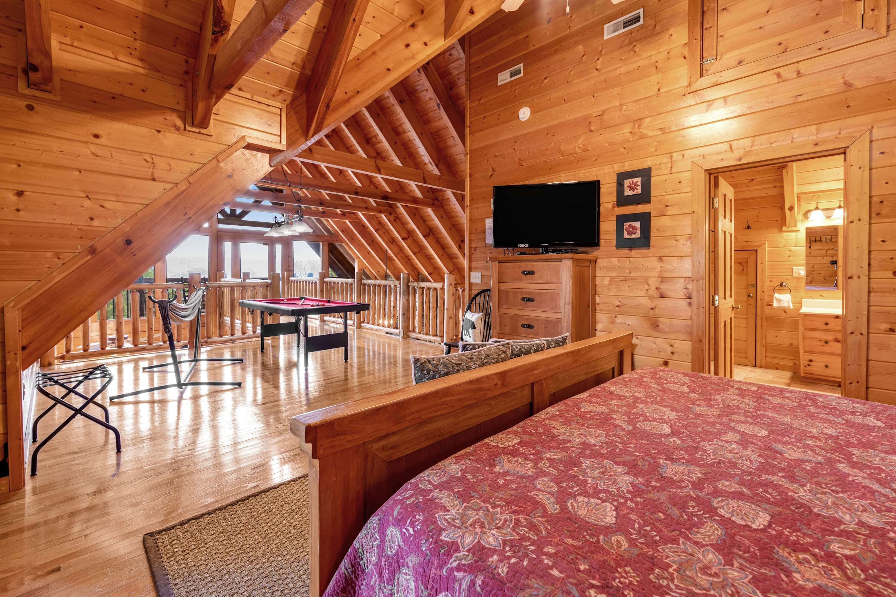 Eine Holzhütte mit Schlafzimmer auf dem Dachboden, einem Essbereich und einem an der Wand befestigten Fernseher.