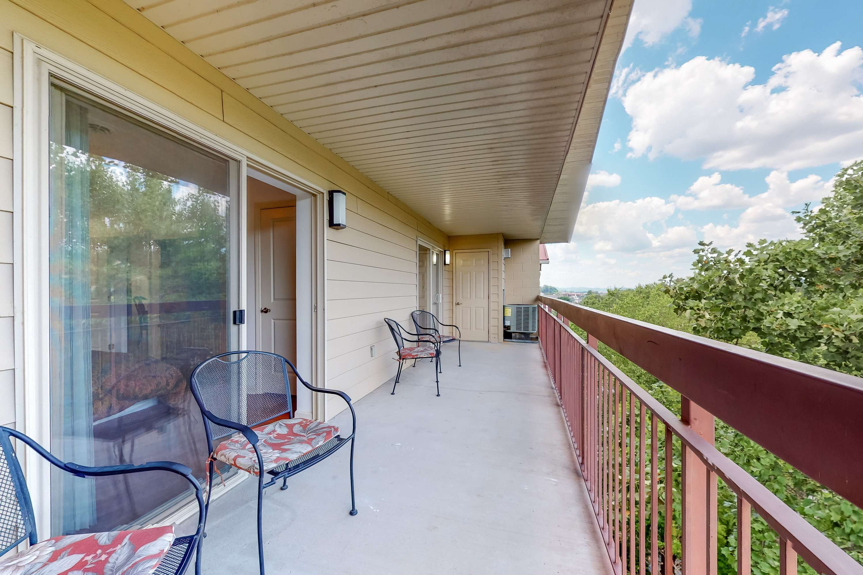 Un balcone coperto con sedie e un tavolo, una porta scorrevole in vetro e vista sul verde.