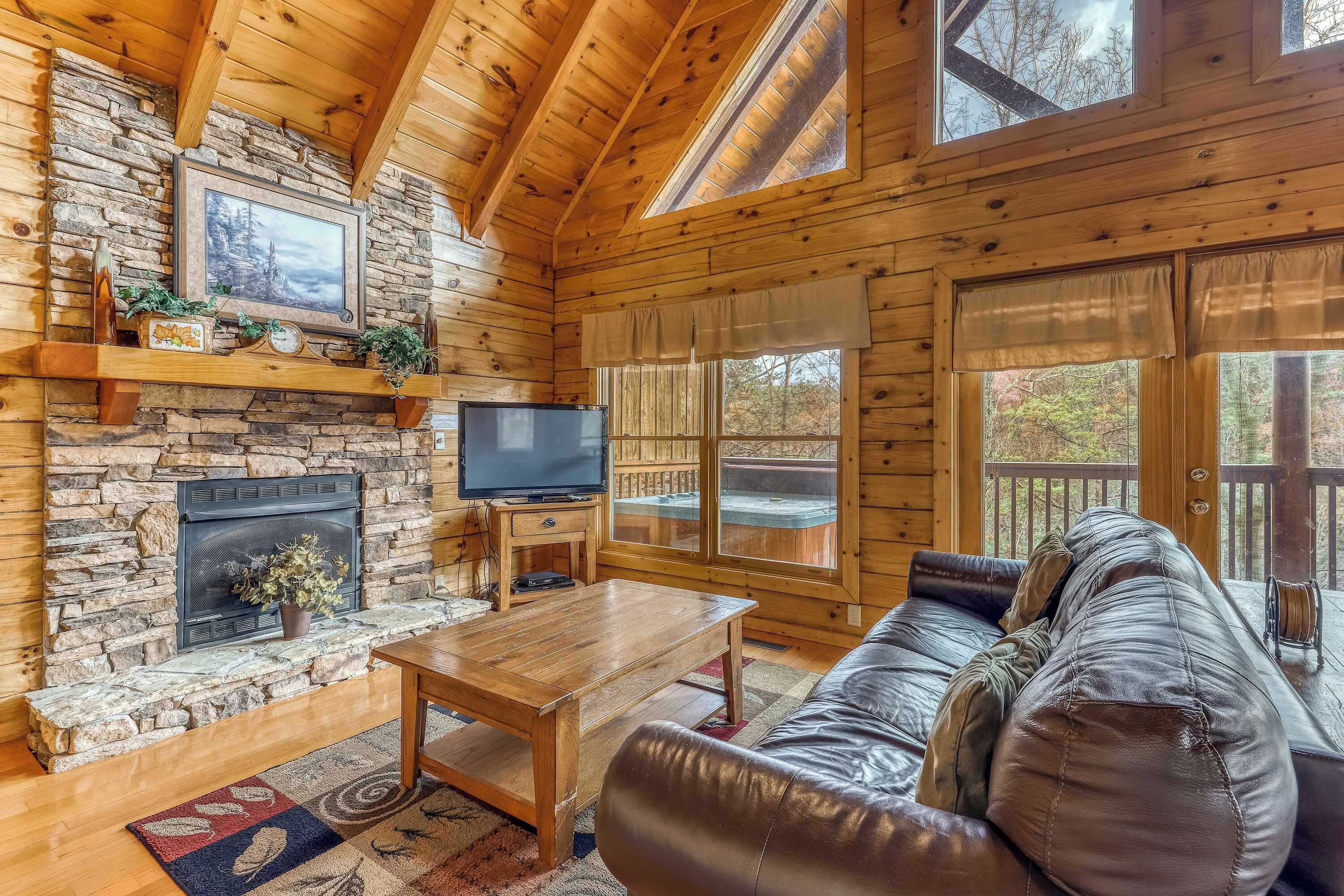A cozy cabin interior with a stone fireplace, wooden walls, a leather sofa, and a television.