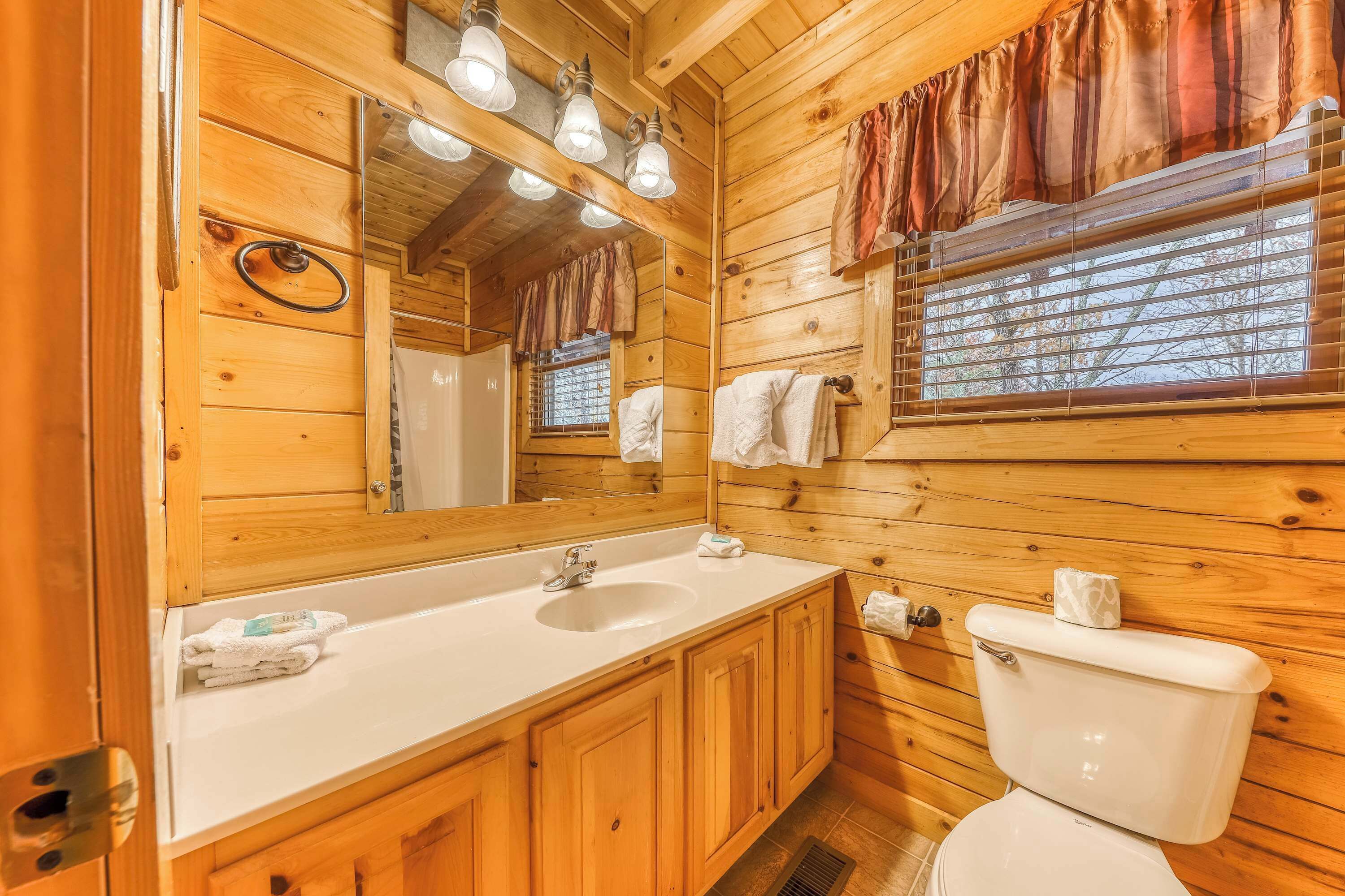 A wooden cabin bathroom with a sink, mirror, and toilet.