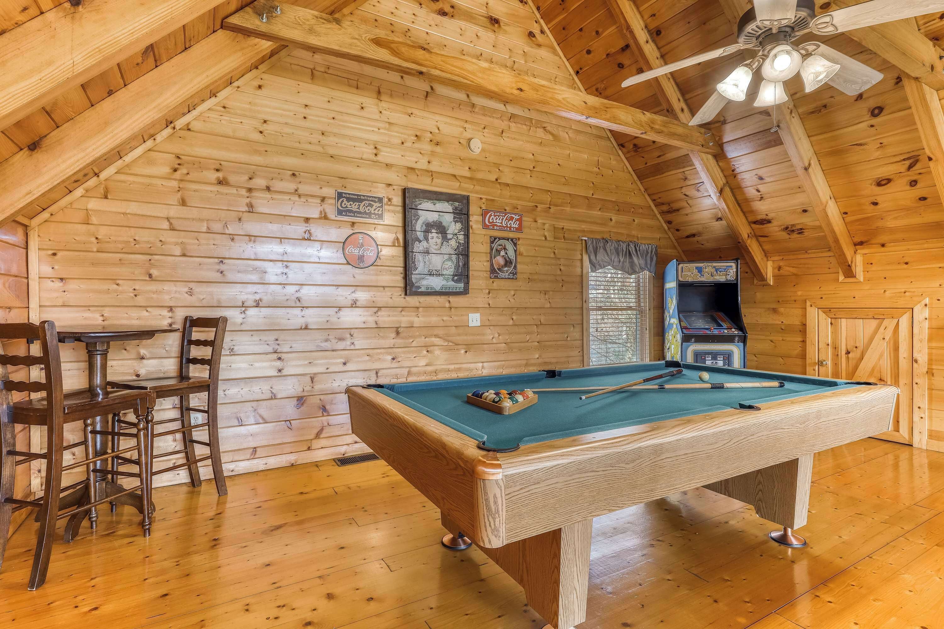 Een kamer met houten lambrisering, een pooltafel, stoelen en een plafondventilator.
