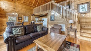 Ein Holzblockhaus-Interieur mit einer Ledersofa, einem Esstisch, einer Treppe und gerahmten Kunstwerken.