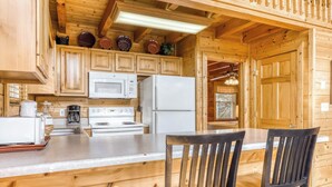 Eine Holzhütte mit einer Küche, inklusive Mikrowelle, Kühlschrank, Herd und Holzschränken.