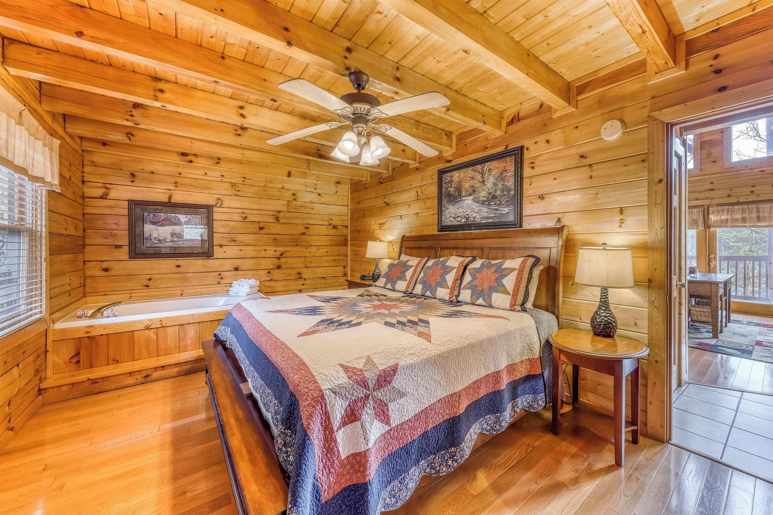 Un dormitorio de cabaña de madera con una cama, un ventilador de techo, una ventana y una puerta.