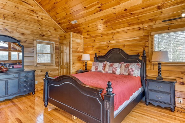 A wooden cabin bedroom with a four-poster bed, a dresser, a nightstand, and a window with blinds.