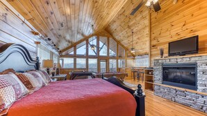 A spacious bedroom with a large bed, a stone fireplace, and a television mounted on the wall. - Family Friendly Luxe Mtn Getaway・Near Downtown (Pigeon Forge)