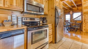 A kitchen with wooden cabinets, stainless steel appliances, and a dining area with a table and chairs. - Family Friendly Luxe Mtn Getaway・Near Downtown (Pigeon Forge)