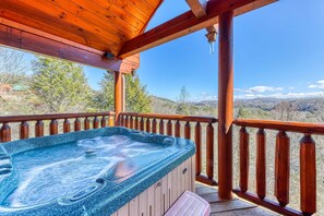 A hot tub on a wooden deck with a wooden railing, overlooking a mountainous landscape.