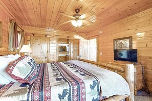 A wooden cabin room with a bed, a ceiling fan, a television, and a window. - Gorgeous Private Oasis, Sleeps 4・Scenic Deck・Games (Sevierville)