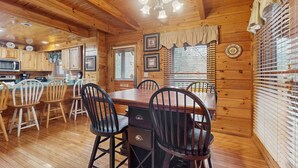 L’intérieur d’un chalet en bois comprend un coin repas, une cuisine et une grande fenêtre équipée de stores.