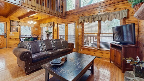 L’intérieur d’un chalet accueillant, avec un plancher en bois, un canapé, une table basse, un téléviseur et un balcon doté d’une balustrade.