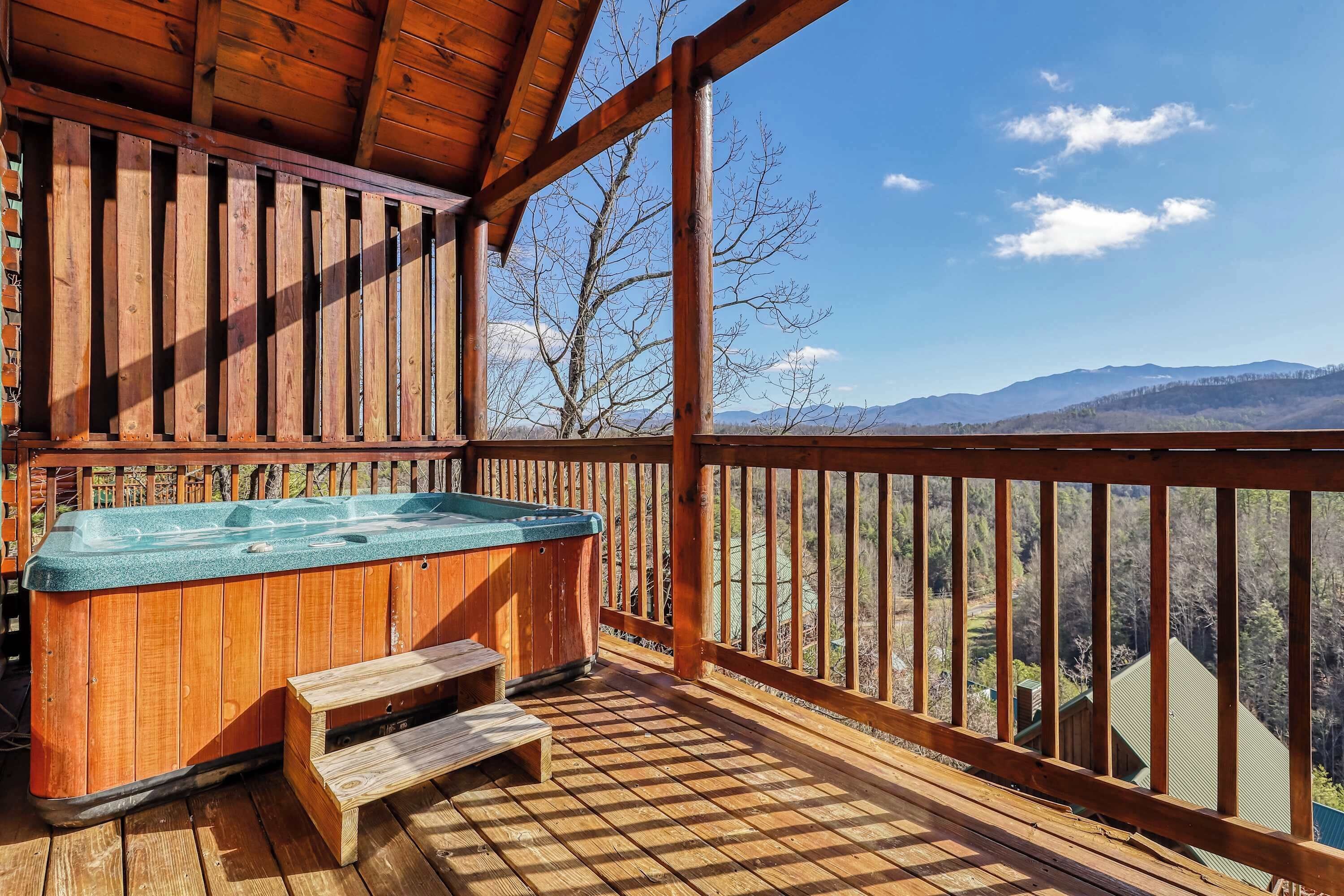 Un terrazzo in legno con una vasca idromassaggio e una panca, affacciato su un paesaggio montuoso.